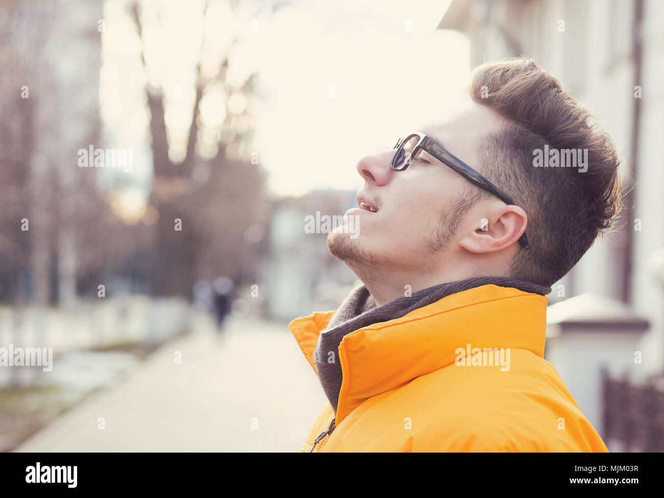 Vista laterale di spensierata giovane uomo in occhiali respirazione profonda permanente sulla strada per godersi la vita. Foto Stock