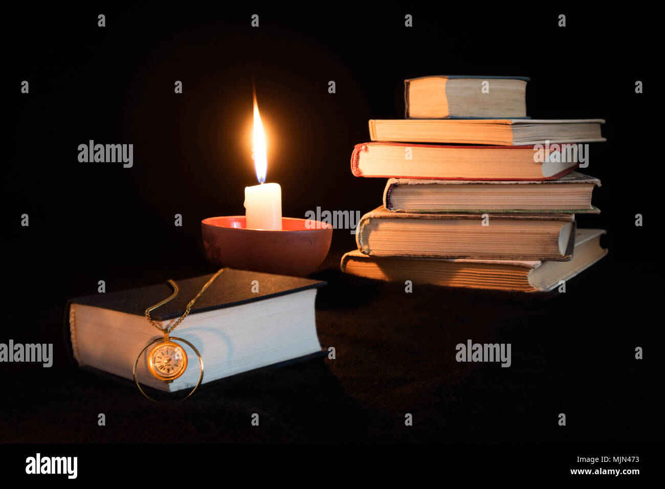 Ancora vita su sfondo nero con libri impilati, candela e unico libro sul  primo piano su