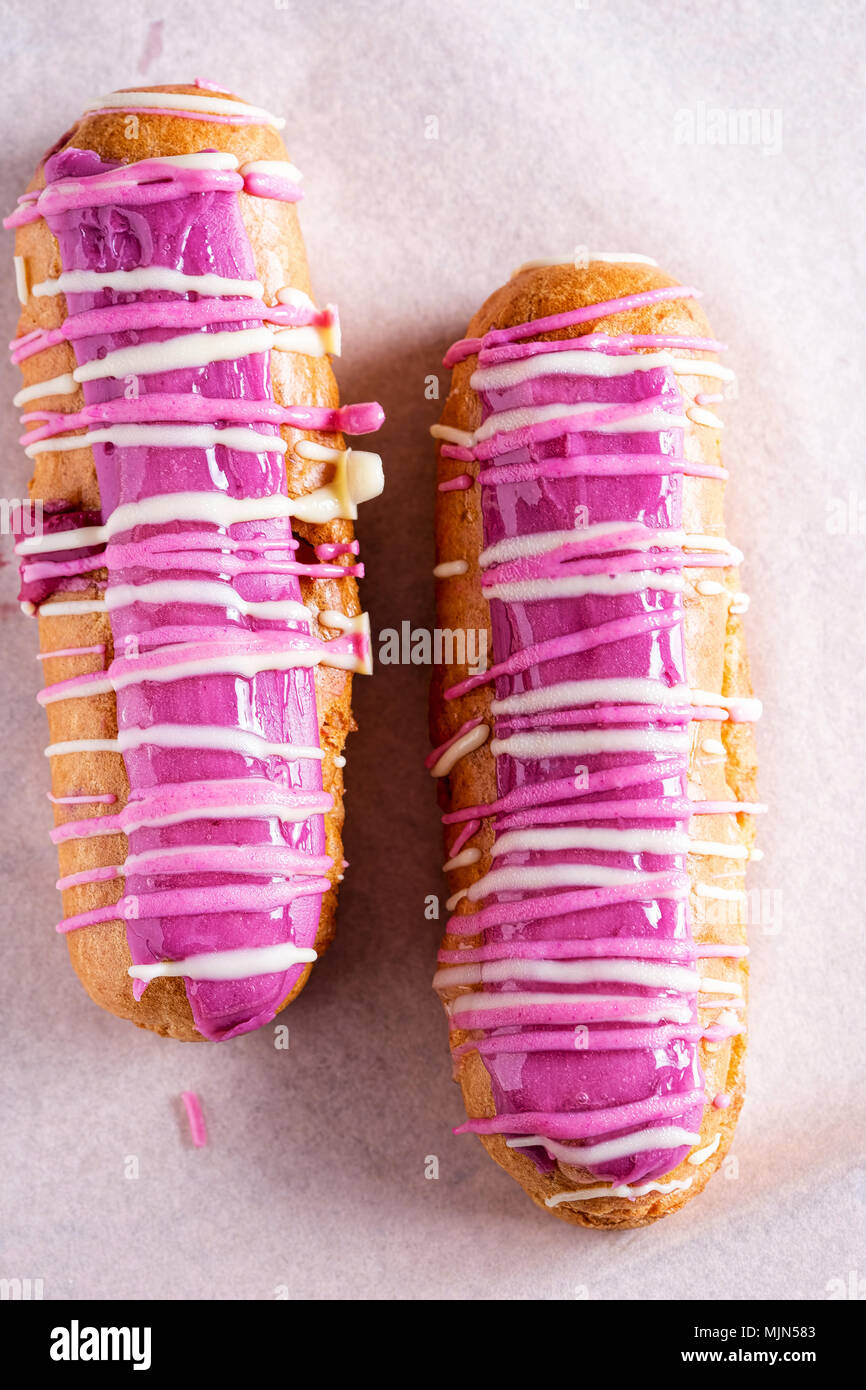 Eclairs ribes nero. Choux pasticcini con crema di ribes nero pasticceria, guarnita con ribes nero e bianco il cioccolato fondente, & smalto Foto Stock