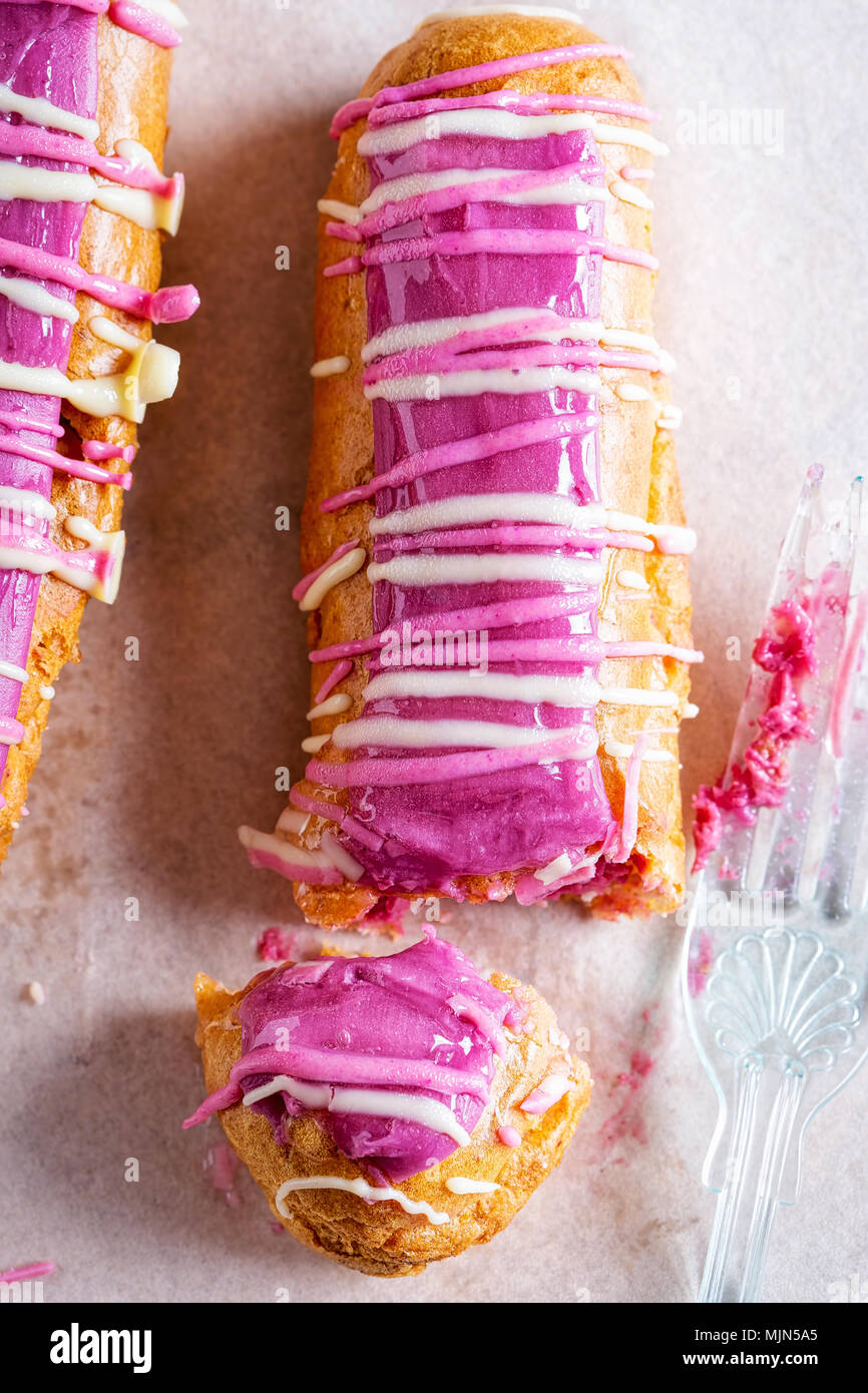 Eclairs ribes nero. Choux pasticcini con crema di ribes nero pasticceria, guarnita con ribes nero e bianco il cioccolato fondente, & smalto Foto Stock