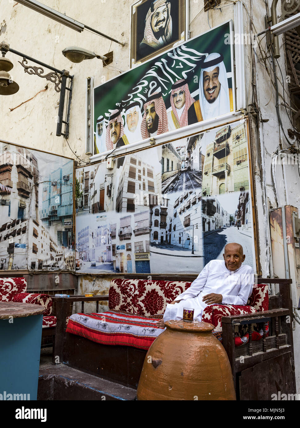 Uomo relax su angolo di strada lettino incorniciata da un murale di fotografia con le immagini di re Salman e Principe Ereditario Salman di Jeddah, Arabia Saudita Foto Stock