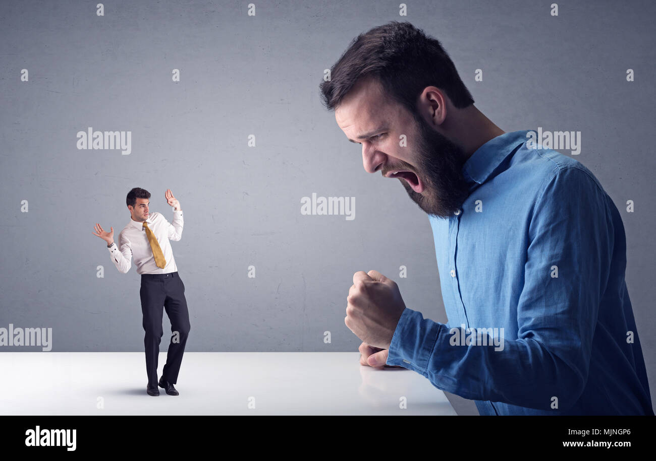 Giovane imprenditore professionale essendo arrabbiato con un altro imprenditore in miniatura di fronte a uno sfondo grigio Foto Stock
