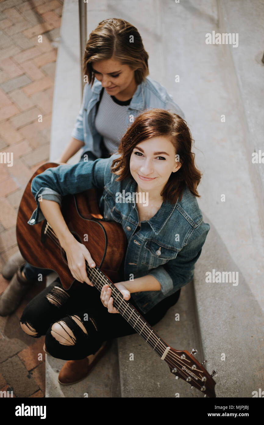 Carino femmina giovani musicisti amici ragazza ridere e cantare sulla città urbana Street passi al di fuori su di una bella giornata d'Autunno Foto Stock