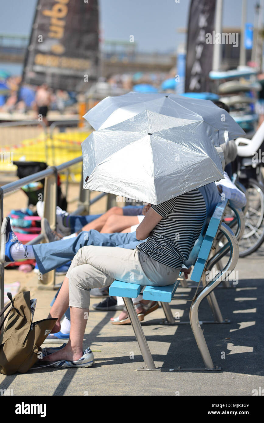 Boscombe, Bournemouth Dorset, Regno Unito, 6 maggio 2018, meteo: sole mattutino sulla costa sud su quello che potrebbe essere il più caldo Mayday bank holiday weekend sul record. La Gente seduta sul lungomare di argento sotto gli ombrelloni. Foto Stock