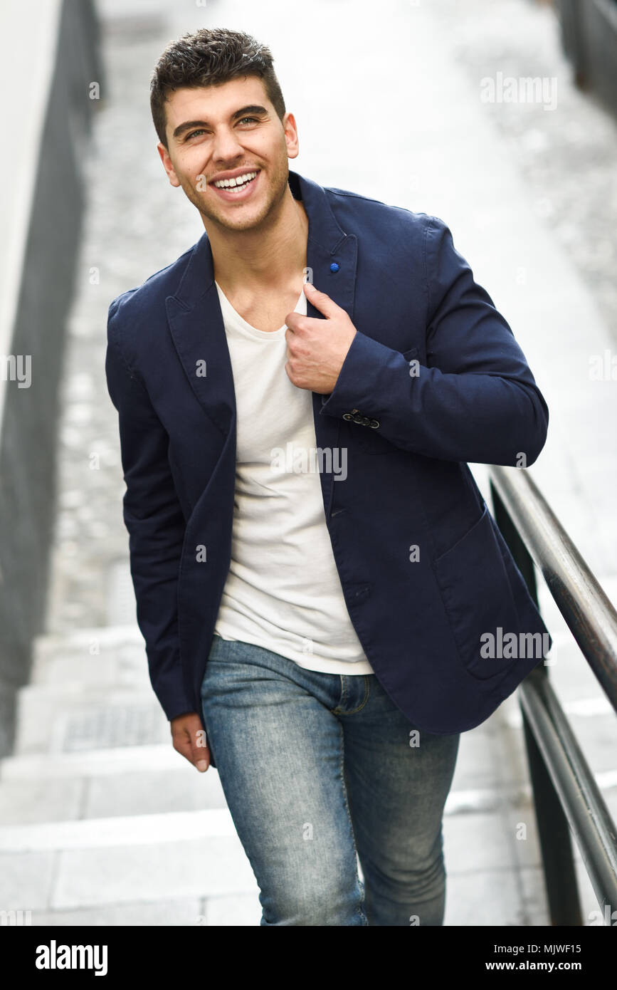 Bel giovane uomo sorridente con gli occhi blu in strada. Modello di moda  passeggiate in background urbano bianco che indossa la t-shirt, jeans e  giacca blu Foto stock - Alamy