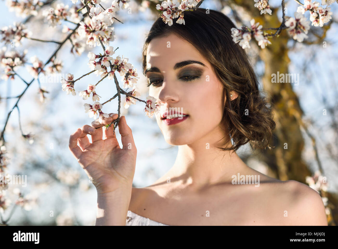 Ritratto di giovane donna nel giardino fiorito in primavera. Fiori di mandorlo fiorisce. Ragazza vestita di bianco come una sposa. Foto Stock