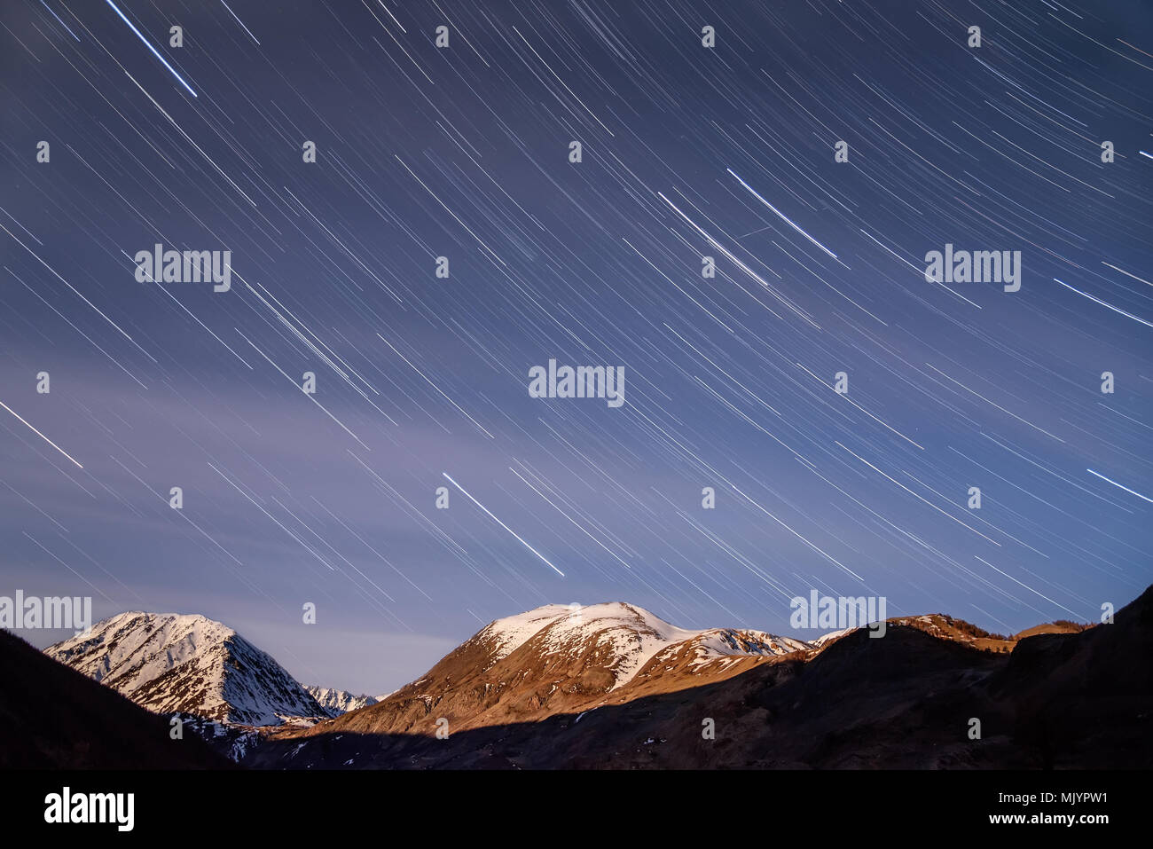 Bella tracce di stelle in forma di binari e sfocata nuvole sull'azzurro del cielo notturno contro lo sfondo delle vette innevate, girato in la luna piena Foto Stock