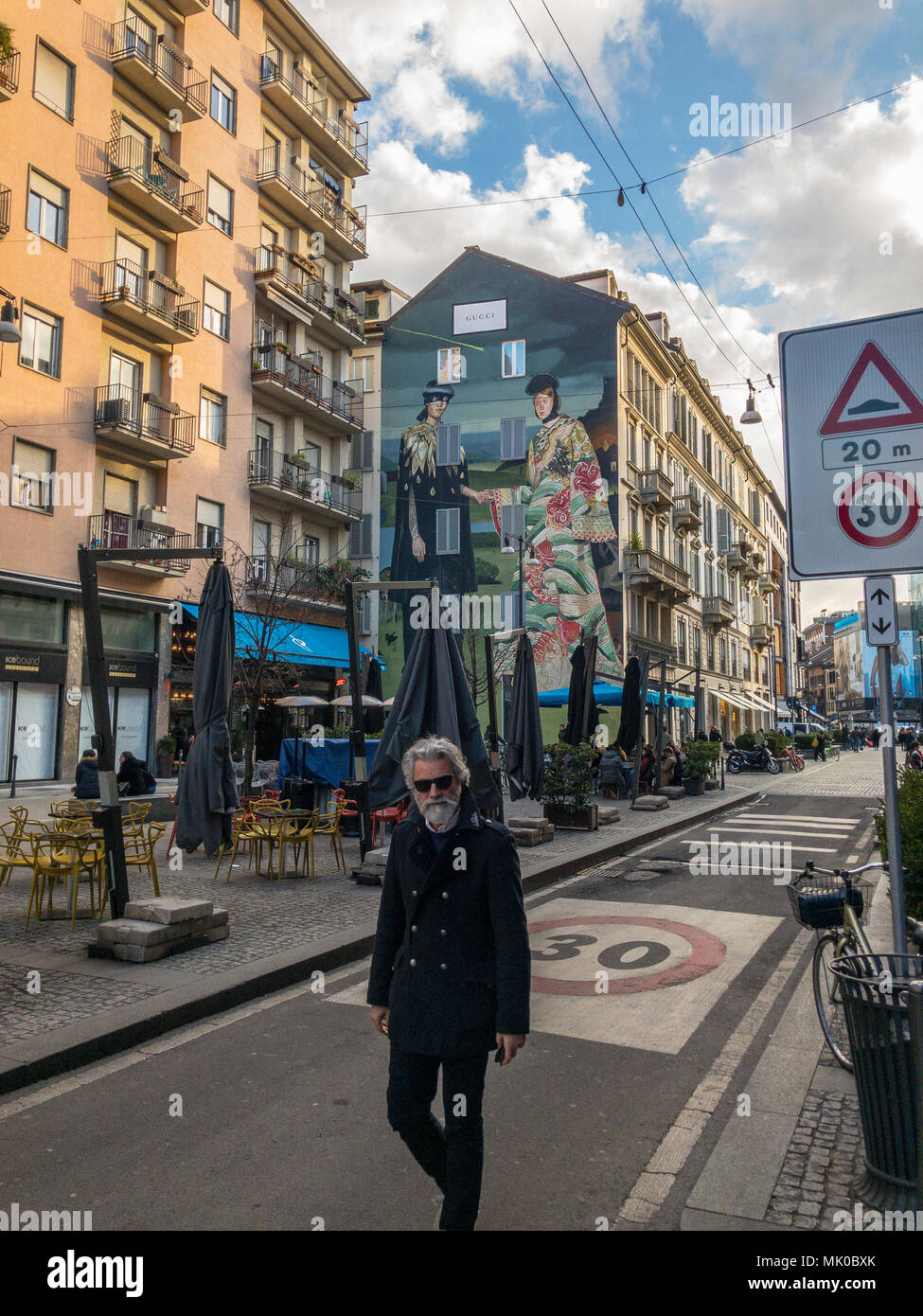 Hipster uomo cammina per le strade del centro di Milano, Corso Garibaldi, Italia. Dietro di lui si può vedere il Gucci poster pubblicitario dipinta su una parete Foto Stock