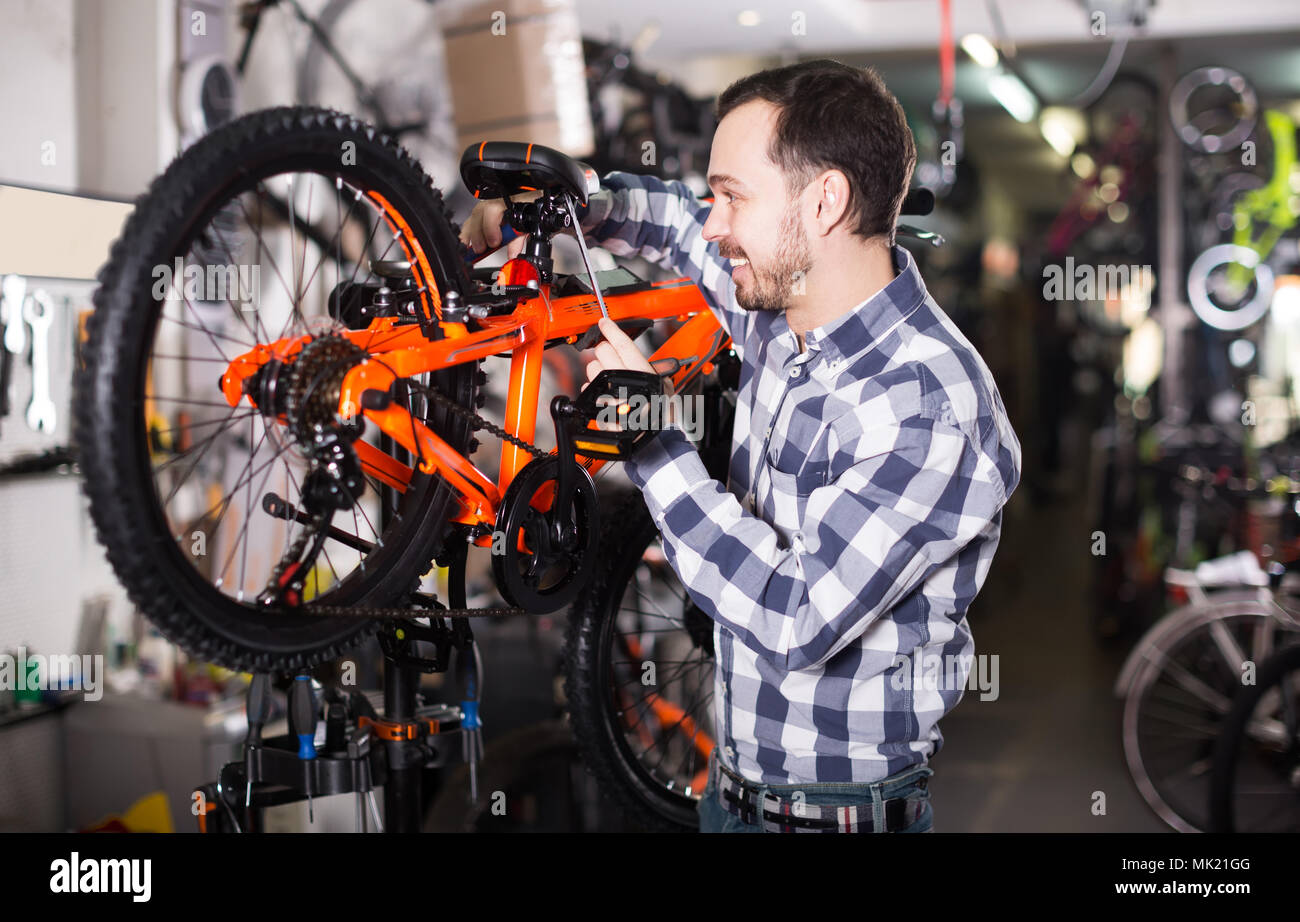 Uomo sorridente fissare il sedile di una moto sportiva in officina per biciclette Foto Stock