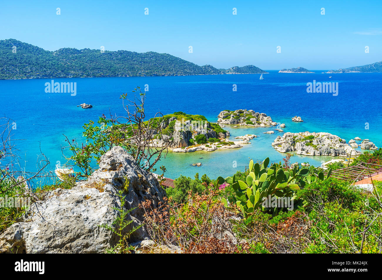 Le isolette rocciose presso la costa di Kalekoy con vegetazione lussureggiante e grandi massi in primo piano, Kekova, Turchia. Foto Stock