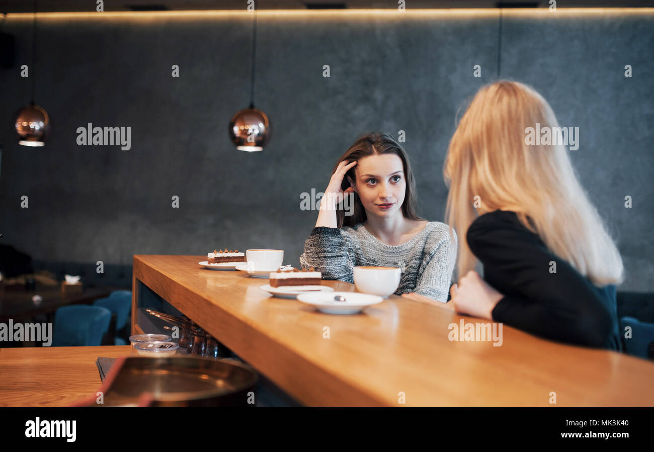 Due gli amici sorseggiando caffè insieme in un negozio di caffè come essi sedersi a un tavolo in chat Foto Stock