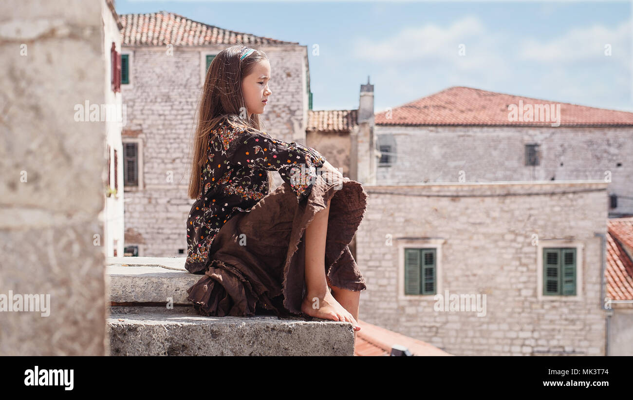 Incantevole piccola ragazza seduta sul tetto di antica costruzione in pietra nella parte vecchia della citta'. Foto Stock