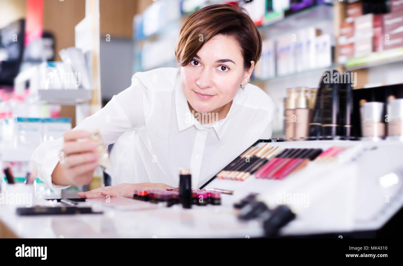 Donna sorridente alla ricerca di make-up di elementi in farmacia Foto Stock