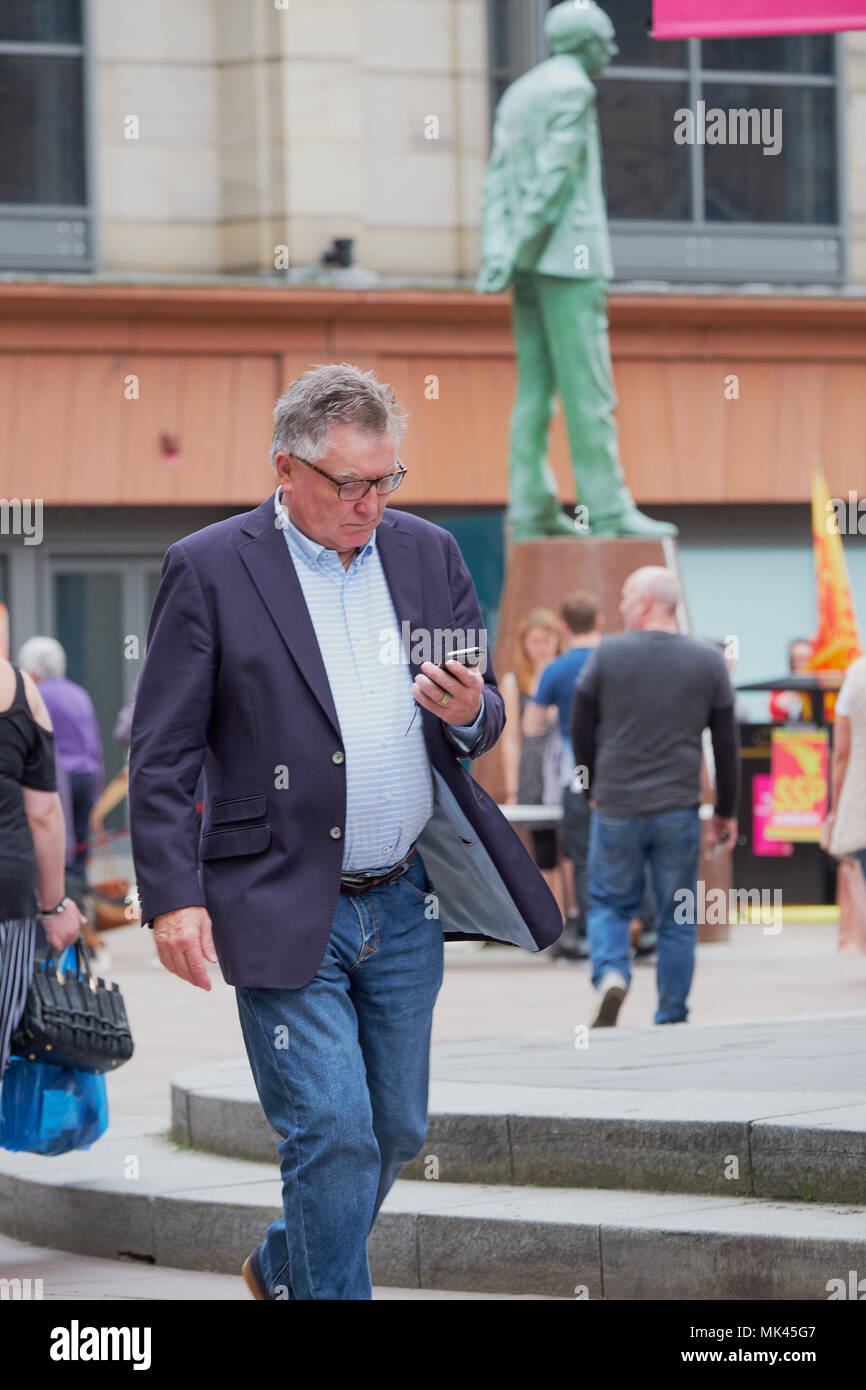 Uomo che cammina per la strada, utilizzando il suo telefono cellulare Glasgow Scozia Scotland Foto Stock