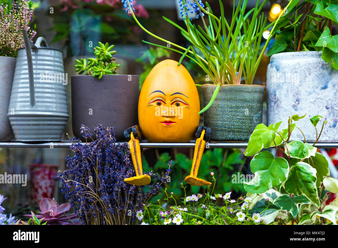 Una figurina di Humpty Dumpty seduto su un ripiano tra piante e vasi di fiori al di fuori di un negozio in Colombia Road Market, London, Regno Unito Foto Stock