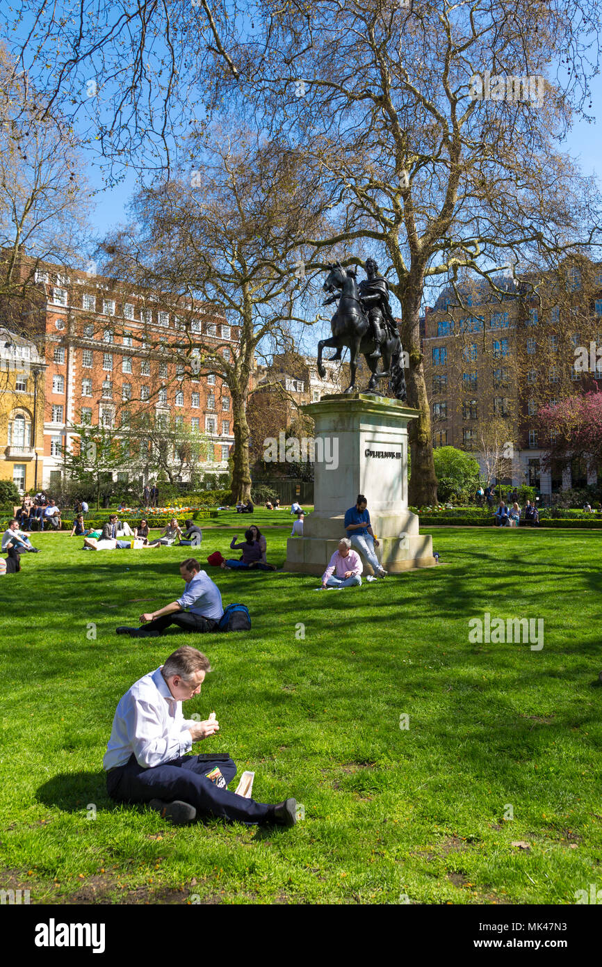 La Gente seduta sul prato e mangiare il pranzo in un piccolo parco cittadino, St James's Square Garden, Londra, Regno Unito Foto Stock
