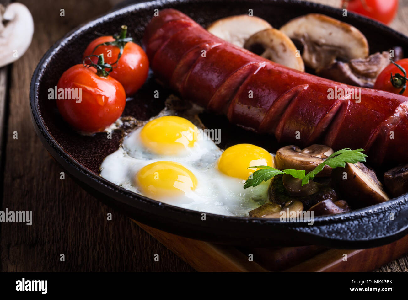 Frittura di uova di quaglia, salsicce, pomodori e funghi in padella in ghisa, prima colazione inglese in stile rustico Foto Stock