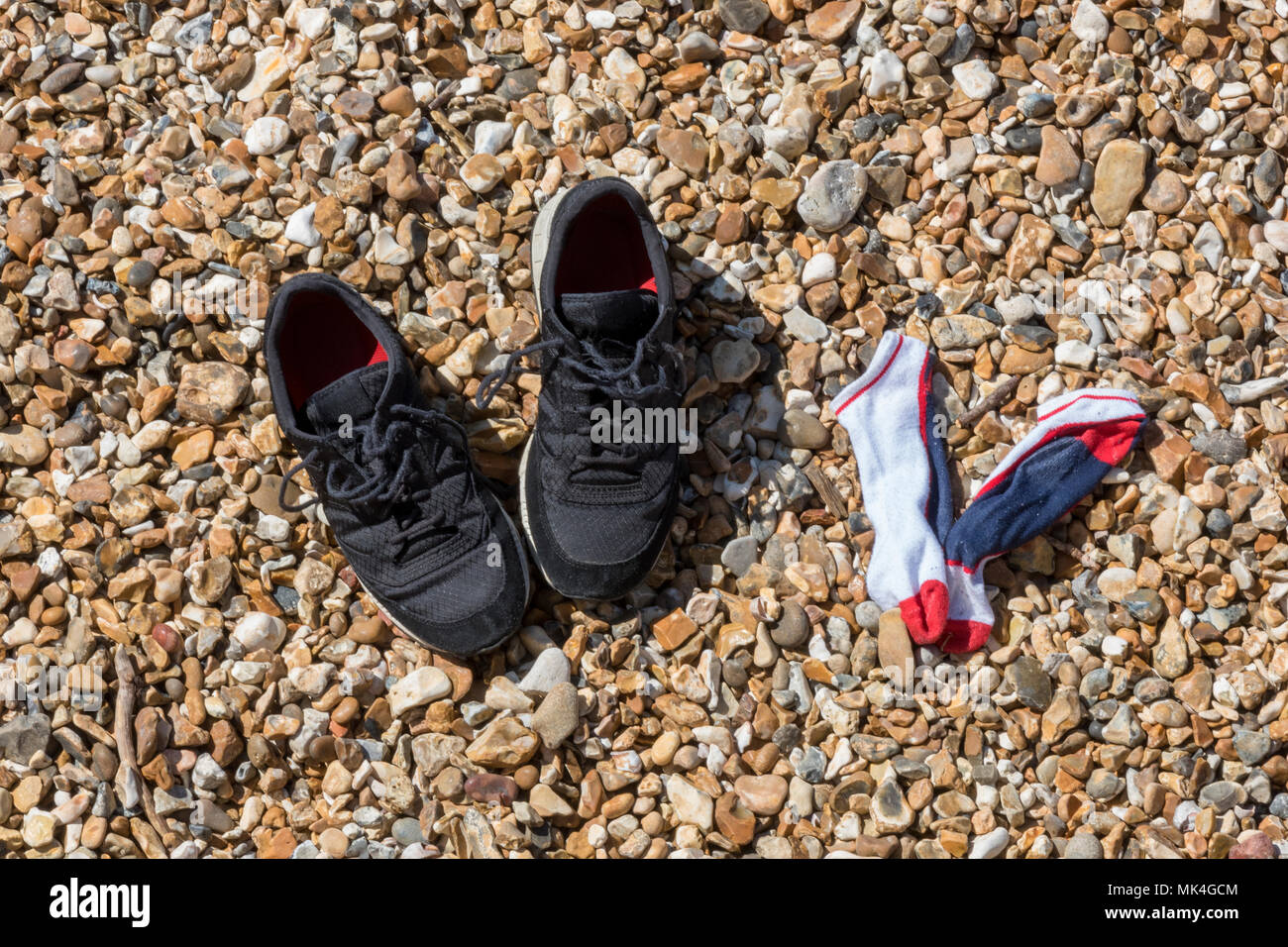 Un po' di allenamento le scarpe e le calze a sinistra su una spiaggia in ghiaia o ciottoli mentre il proprietario è andato a nuotare in mare al mare.tipicamente britannico Foto Stock