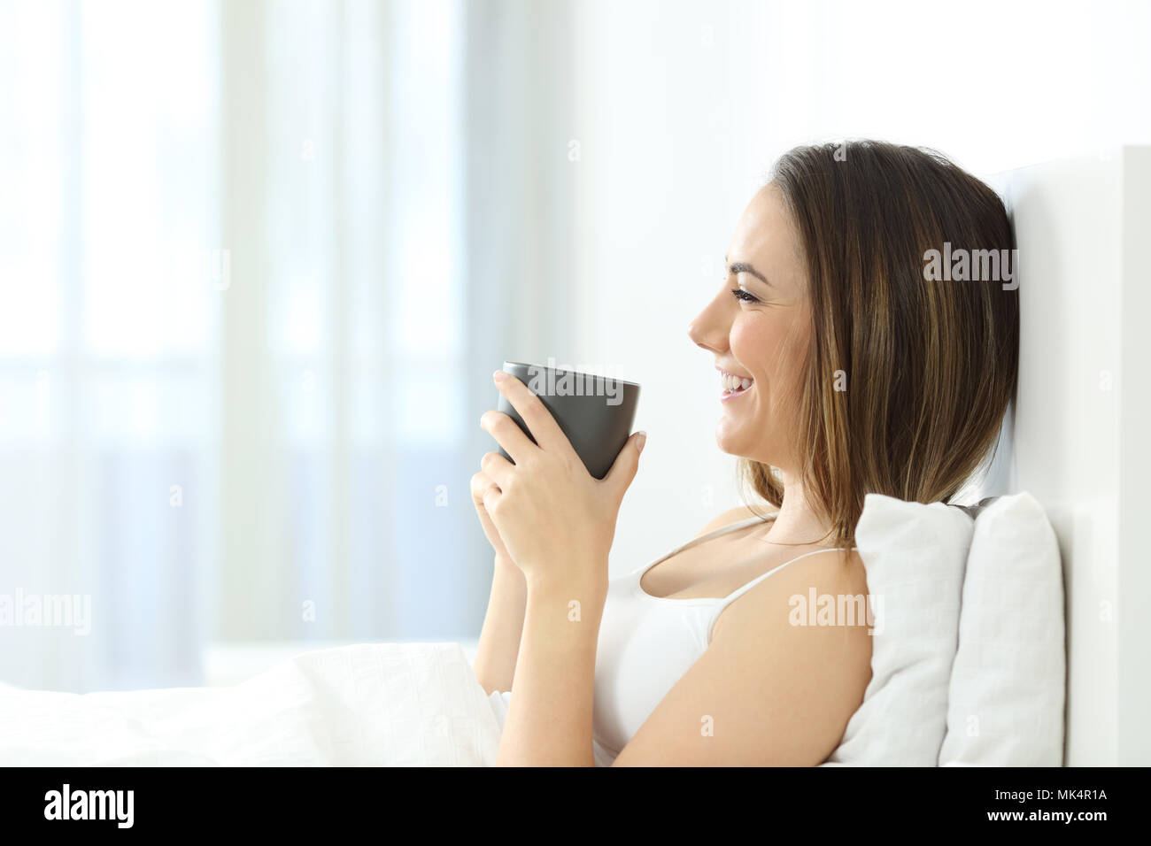 Vista laterale verticale di una ragazza felice risveglio con colazione a letto a casa Foto Stock