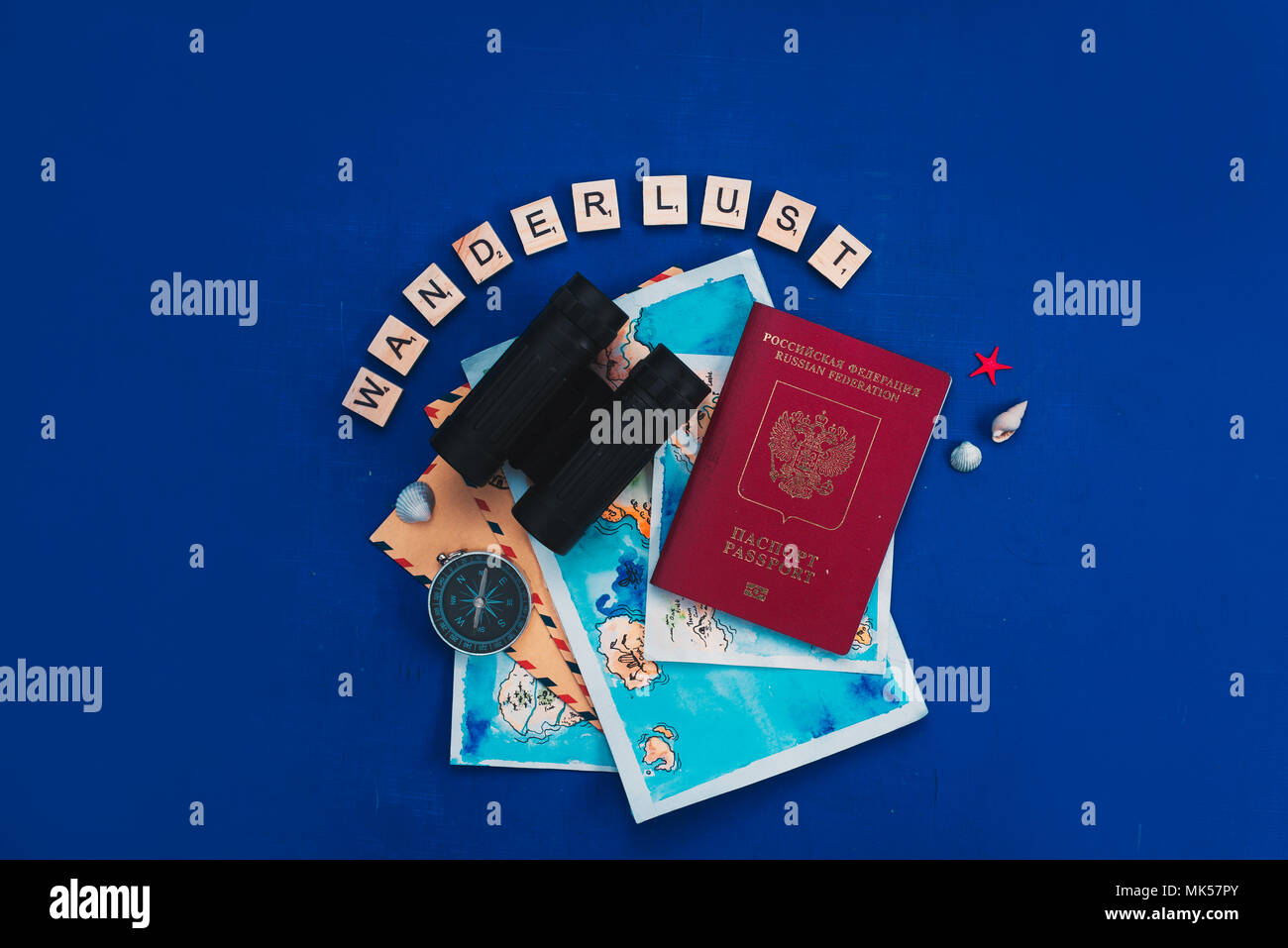 Viaggio di esplorazione e di concetto con mappe ad acquerello, passaporto, Bussola Binocolo, lente di ingrandimento e Wanderlust scrabble lettere. Appartamento di vacanza giacciono su uno sfondo blu scuro con spazio di copia Foto Stock