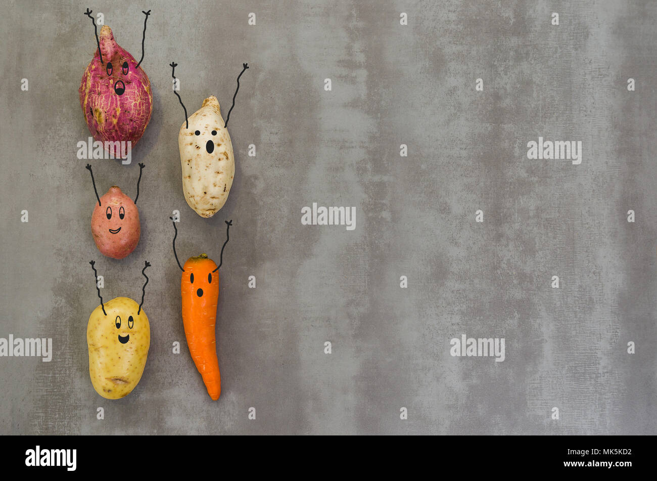 Grande concetto di mangiare sano, verdure con volti felici con le braccia in alto, patate, patata dolce, la carota. Sfondo grigio, in cemento lucidato. Foto Stock