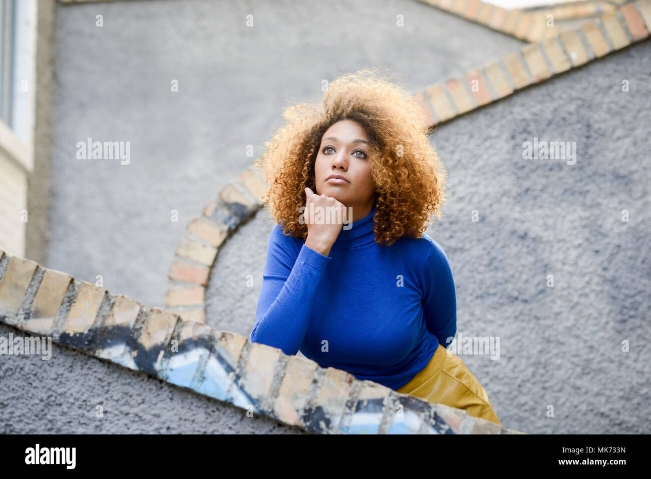 Bella giovane africano donna americana, modello di moda, con acconciatura afro e gli occhi verdi che indossa un maglione blu e giallo gonna in background urbano Foto Stock