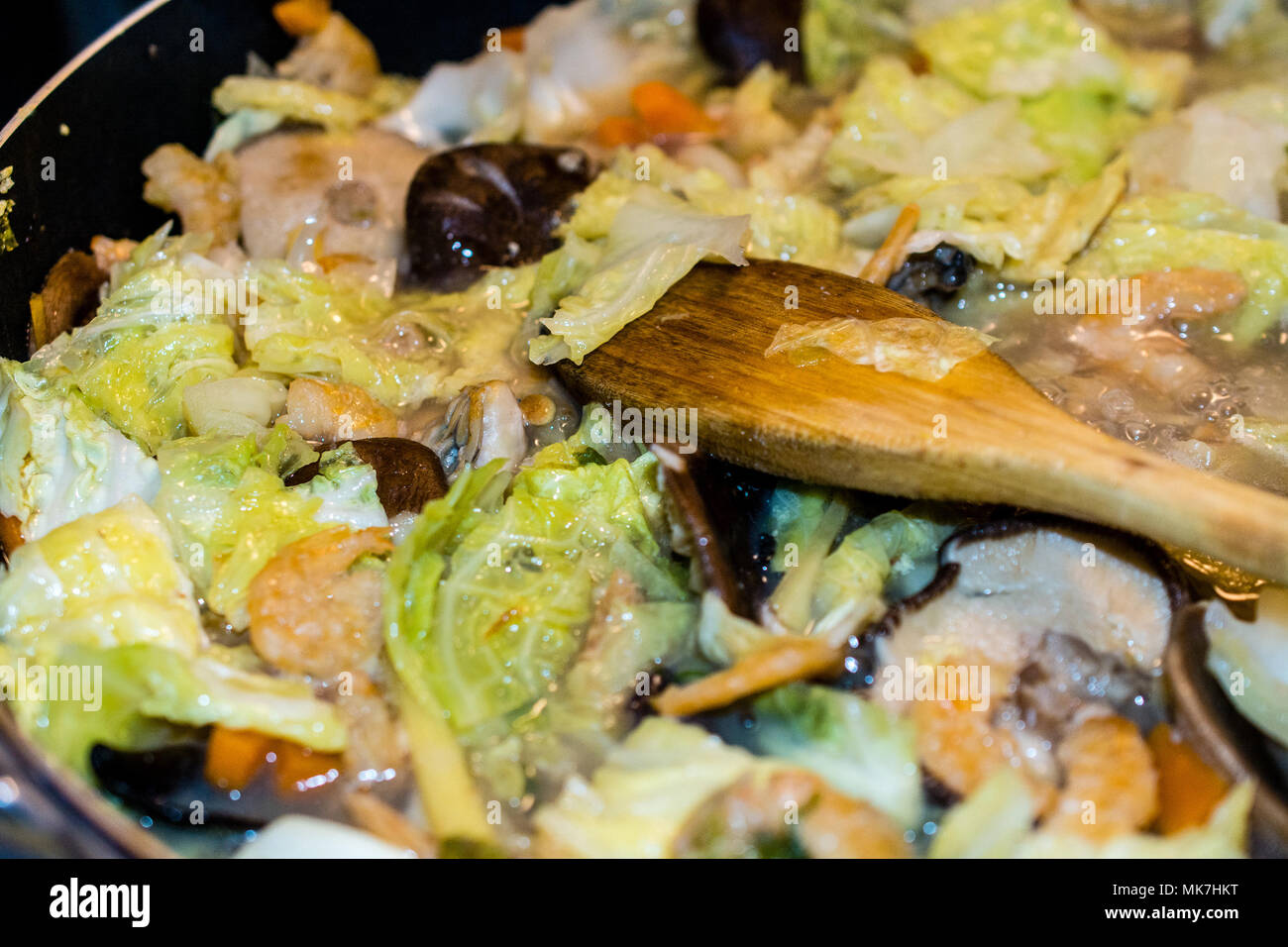 Primo piano sul cucchiaio di legno stirrying brasati Napa cavolo vista dall'alto. Si tratta di un comfort food a Taiwan e in altri paesi asiatici Foto Stock