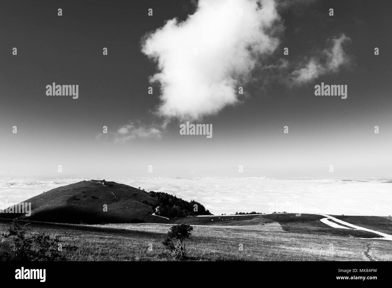 Vista del Monte Subasio (Umbria) sulla valle ricca di nebbia e sotto un ampio cielo con nuvole bianche Foto Stock