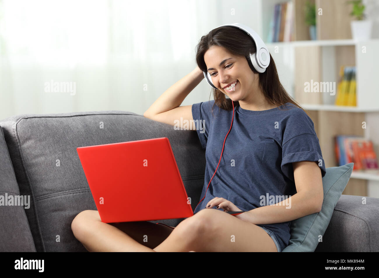 Felice teen di guardare i video online in un computer portatile rossa seduta su un divano nel salotto di casa Foto Stock