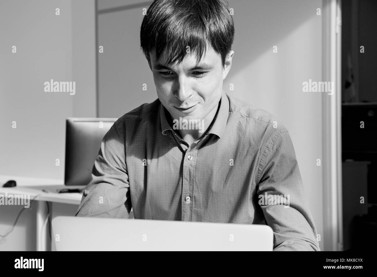 Ritratto in bianco e nero di un uomo smilling davanti a un computer portatile in ufficio. Foto Stock