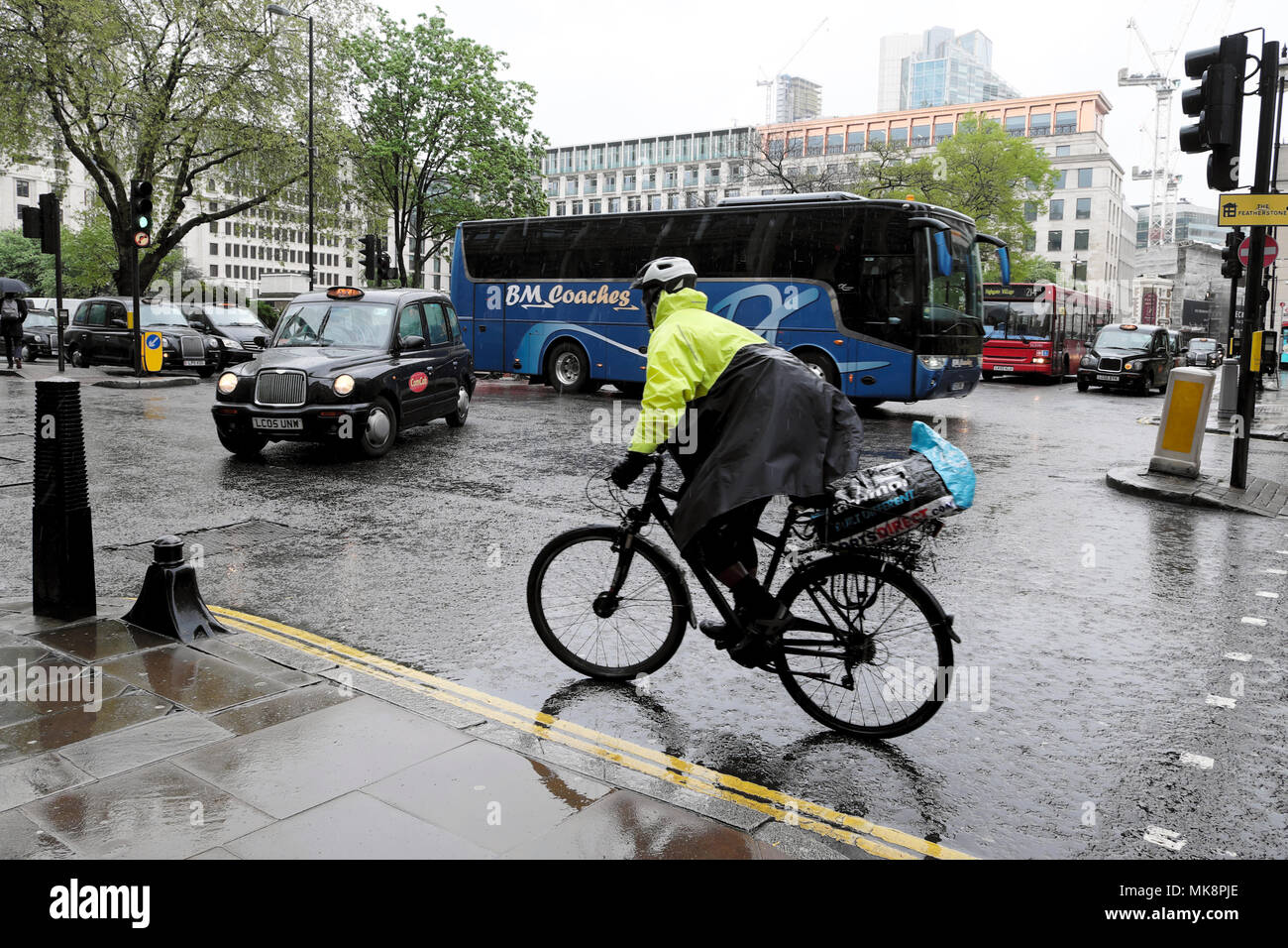 Un maschio ciclista indossando un impermeabile e casco di sicurezza cicli attraverso intersezione semaforo sotto la pioggia su una strada trafficata nella città di Londra UK KATHY DEWITT Foto Stock