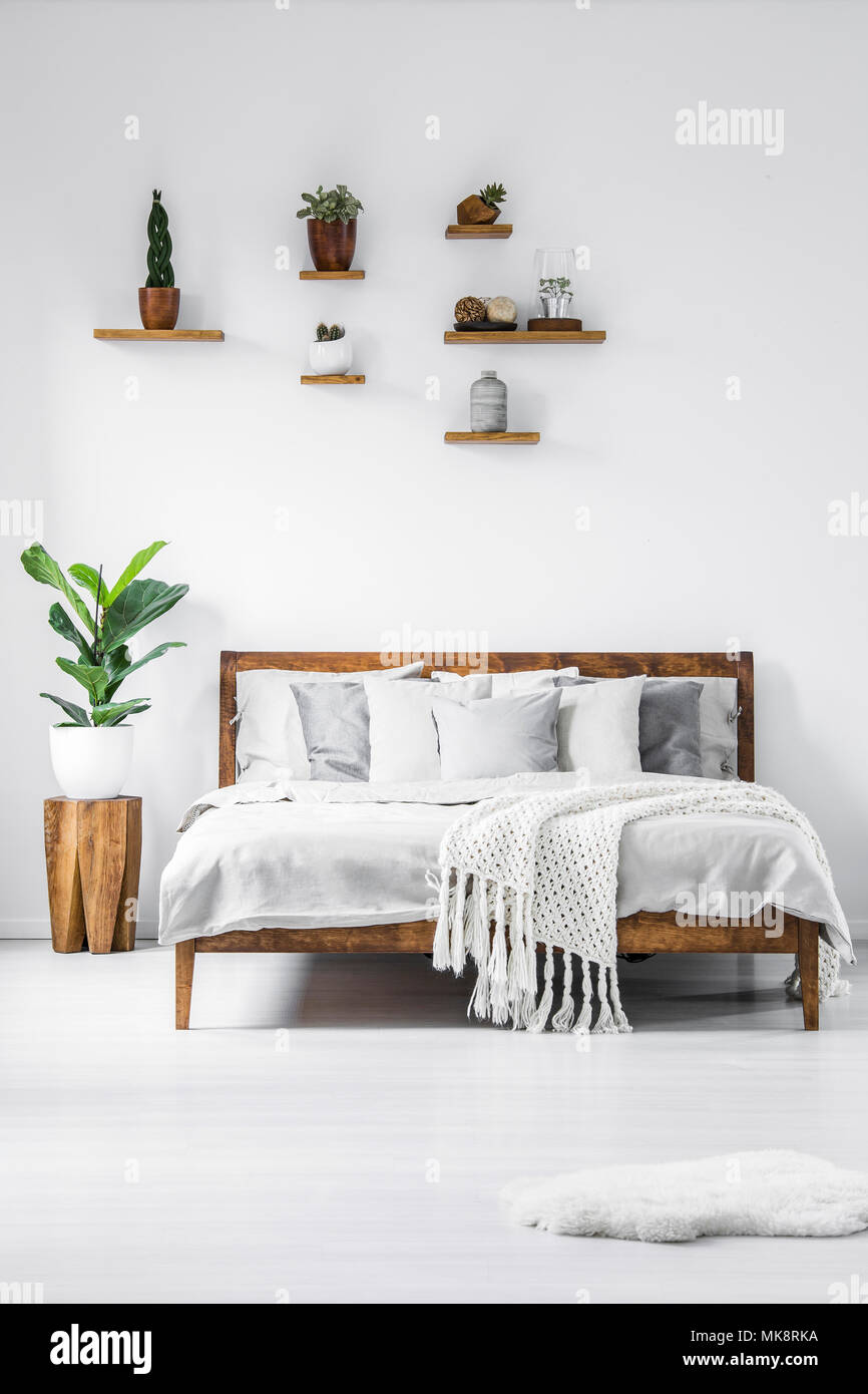 Impianto su uno sgabello di legno accanto al letto in semplice bianco  interiore camera da letto con ripiani Foto stock - Alamy