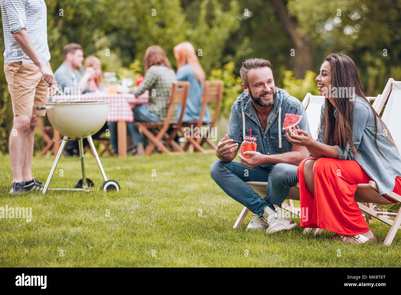 Donna sorridente mangiando anguria e il suo amico a bere un cocktail in giardino durante una festa Foto Stock