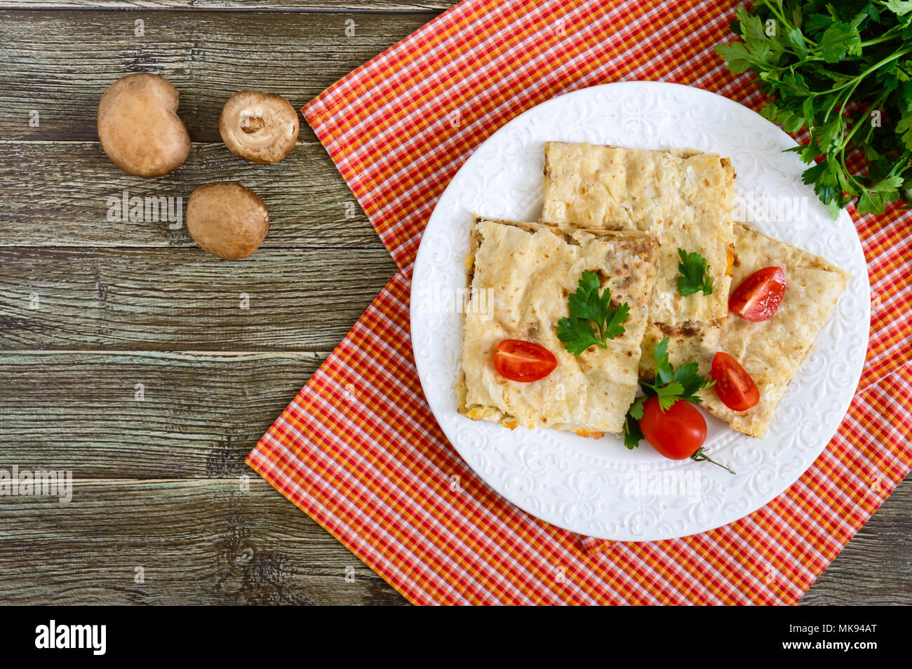 Grafico a torta, casseruola pita con funghi, ricotta e formaggio su una piastra bianca su uno sfondo di legno. Layer Cake. Vista superiore Foto Stock