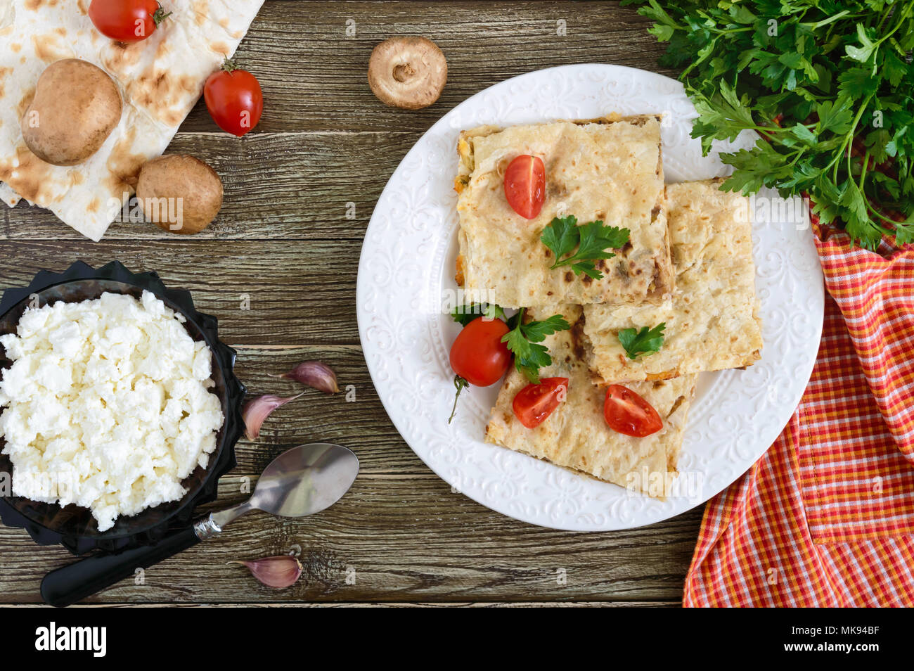 Grafico a torta, casseruola pita con funghi, ricotta e formaggio su una piastra bianca su uno sfondo di legno. Layer Cake. Vista superiore Foto Stock