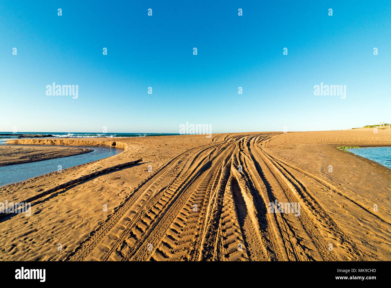 Modelli e texture delle tracce del veicolo sulla spiaggia di sabbia tra estuario contro acqua blu skyline costiera Foto Stock