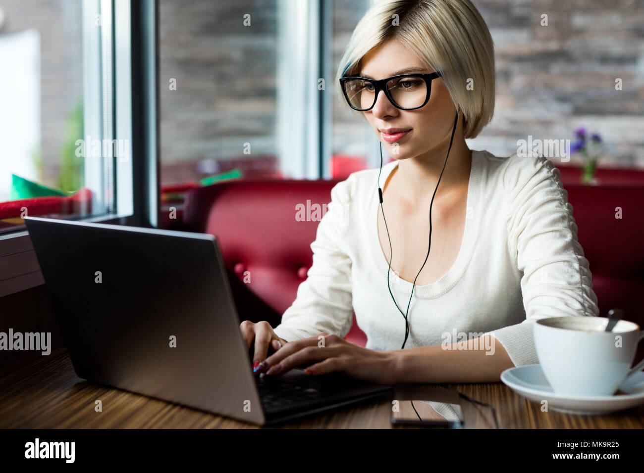 Blogger femmina con gli occhiali durante l'utilizzo di Laptop In Cafe Foto Stock