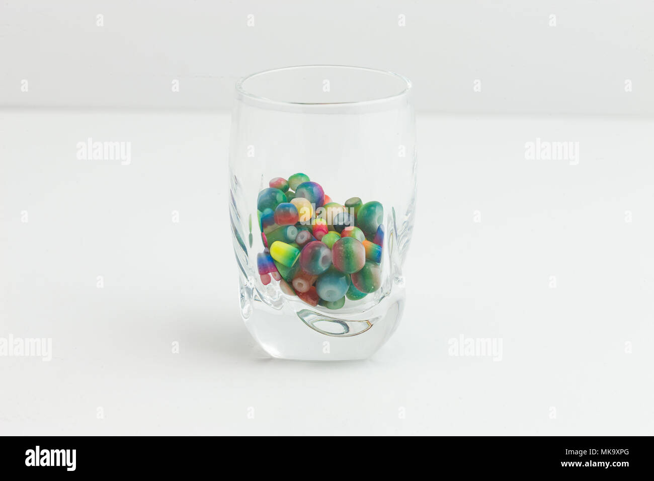 Colorato e sagomato gioielli di perline in un piccolo Vetro Chiaro su bianco Foto Stock