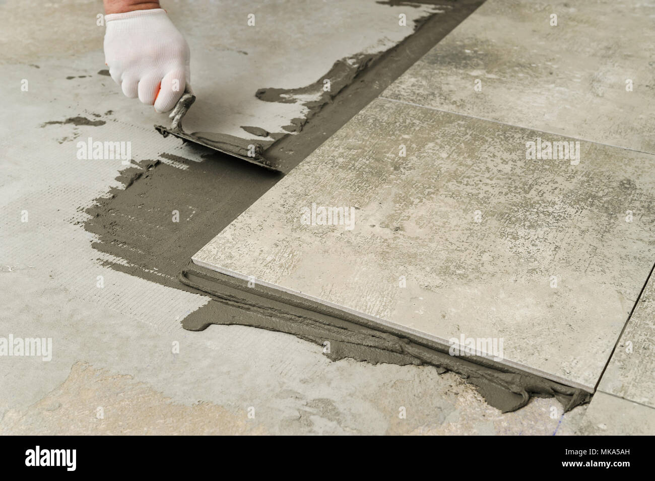 La posa di piastrelle di ceramica. Mortaio Troweling su un pavimento di  cemento in preparazione per la posa di piastrelle per pavimento Foto stock  - Alamy