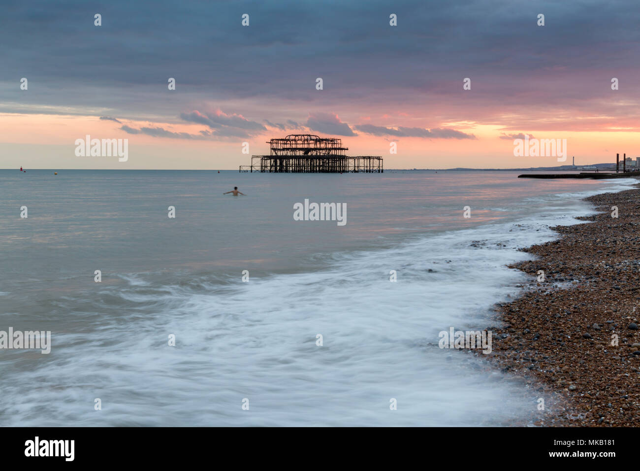 Nuotatore solitario davanti al Molo di Ponente, Brighton East Sussex, Regno Unito durante un mese di luglio il tramonto. Foto Stock