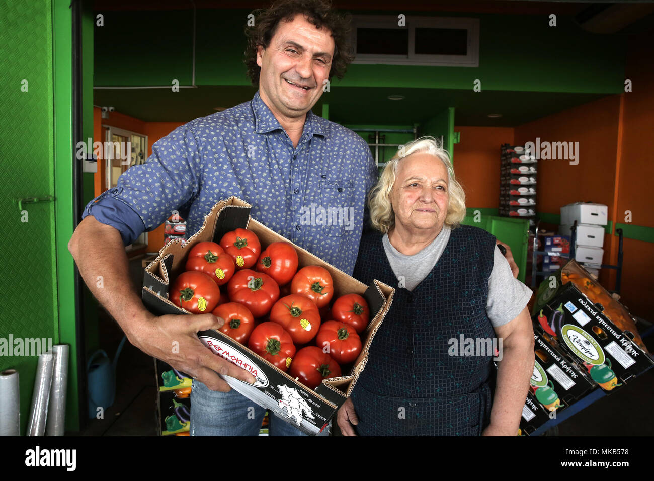 Un grossista in posa per una foto con il suo cliente, un 73-anni vecchia donna, tenendo una cassa di pomodori nella Frutta & Verdura in Atene, greco Foto Stock