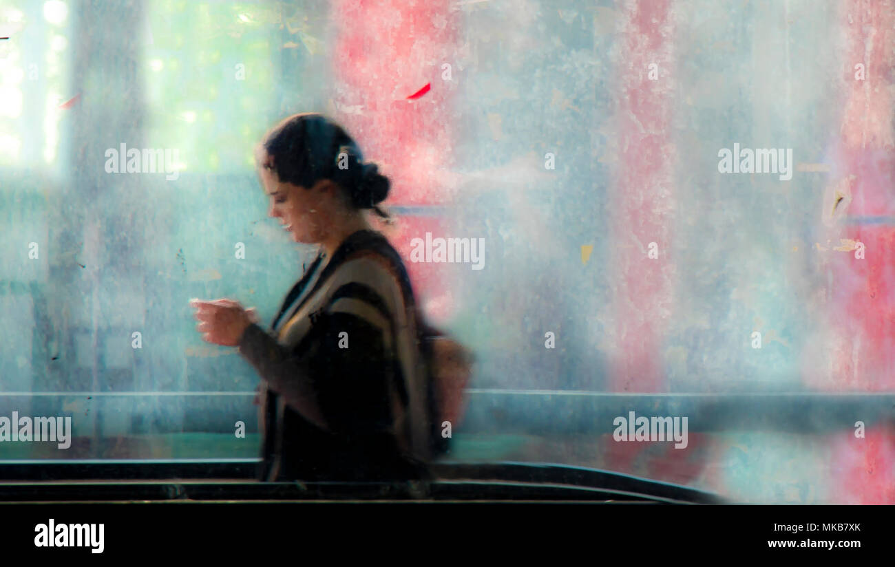 Belgrado, Serbia - 11 Aprile 2018: sfocata giovane donna guardando il telefono e a piedi al di fuori del passaggio della metropolitana e di un traffico in movimento dietro di lei, wit Foto Stock