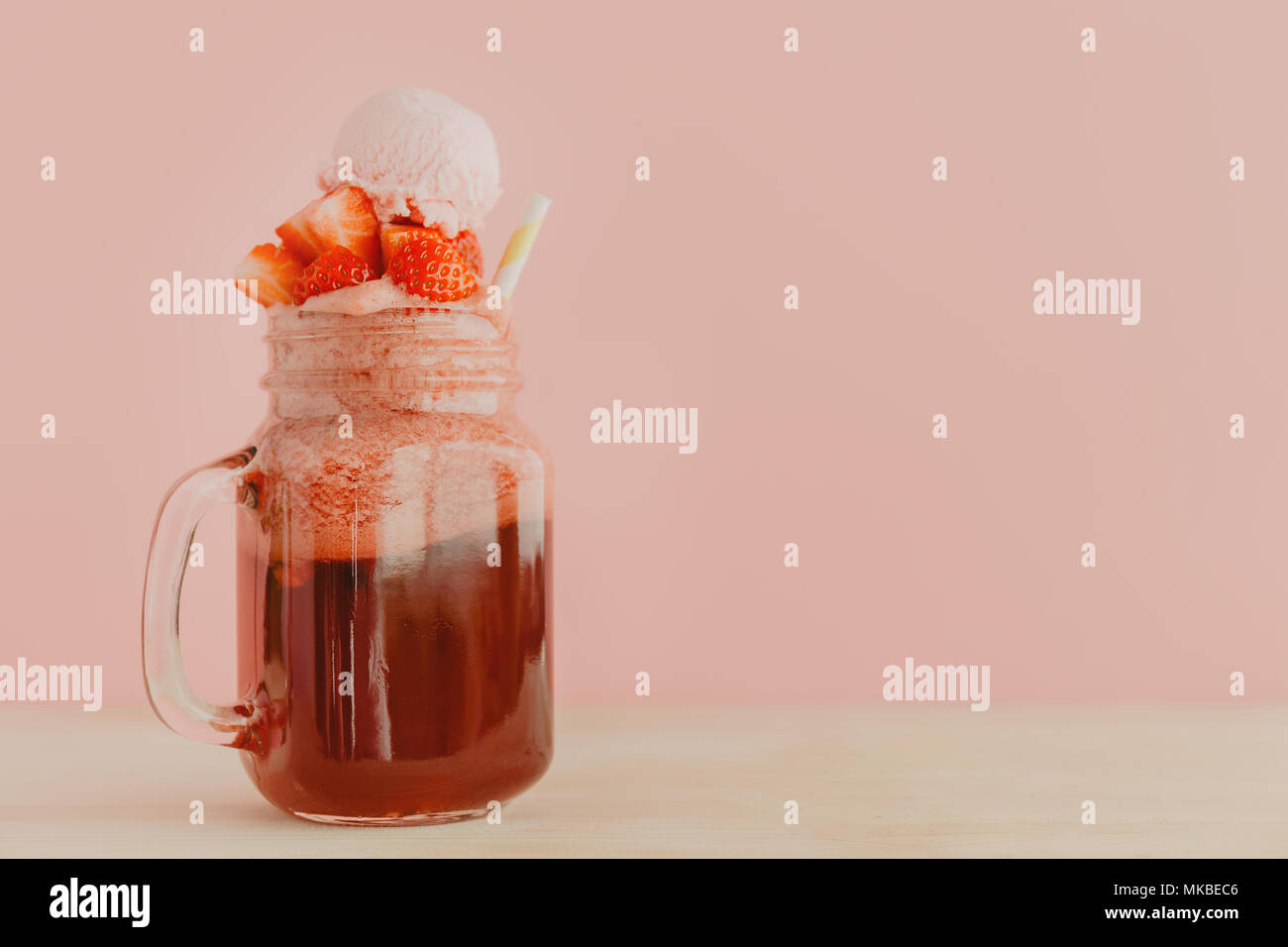 Vaso di vetro con colore rosso brillante limonata fatta di fragole guarnito con frutti di bosco e servite con paglia in rosa. Foto Stock