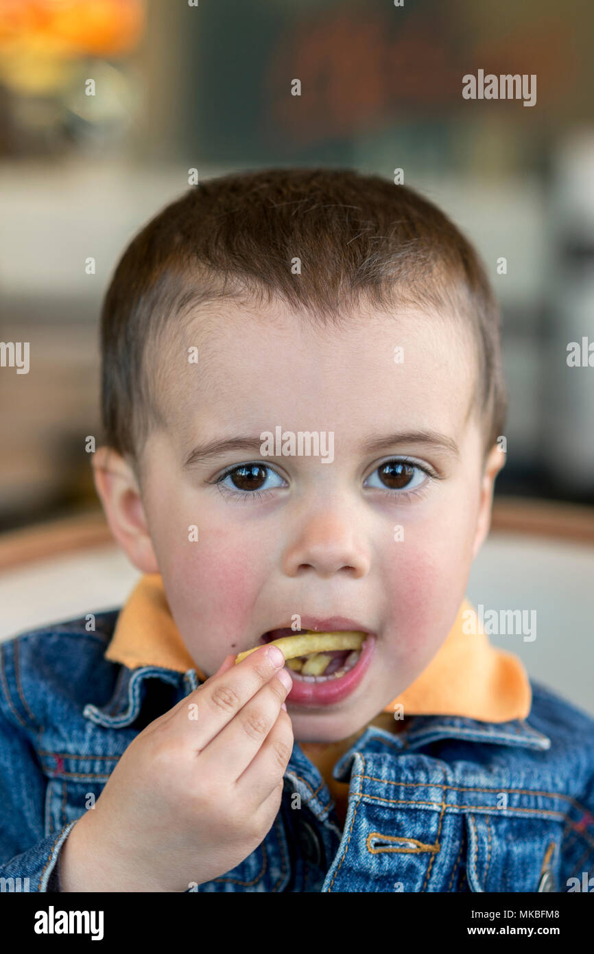 Un happy baby boy mangia le patatine fritte. fast food. Europeo. boy 2 anni  di close-up di mangiare patatine fritte. Carino piccolo bimbo seduto presso  il cafe mangiare tas Foto stock -