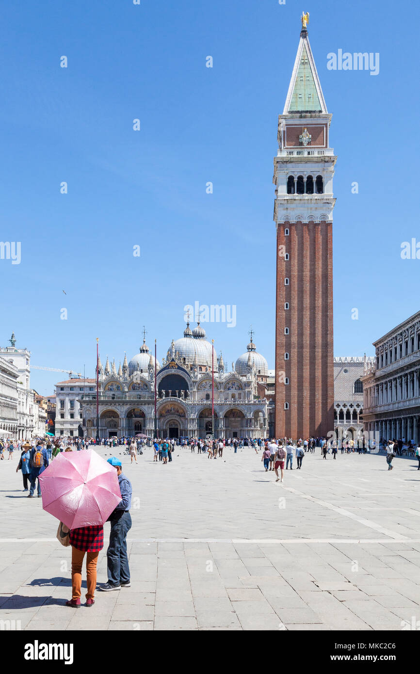 Donna con ombrello rosa nella parte anteriore del St Marks Cattedrale e il Campanile di Piazza San Marco, Venezia, Veneto, Italia con i turisti in background Foto Stock