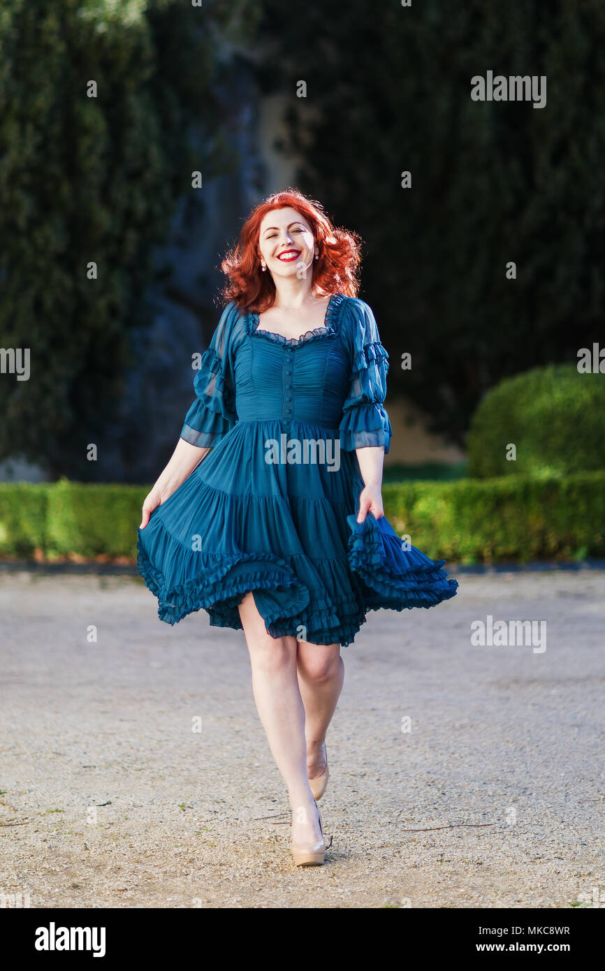 Felice redheaded donna cammina in un parco con abito fluente Foto Stock