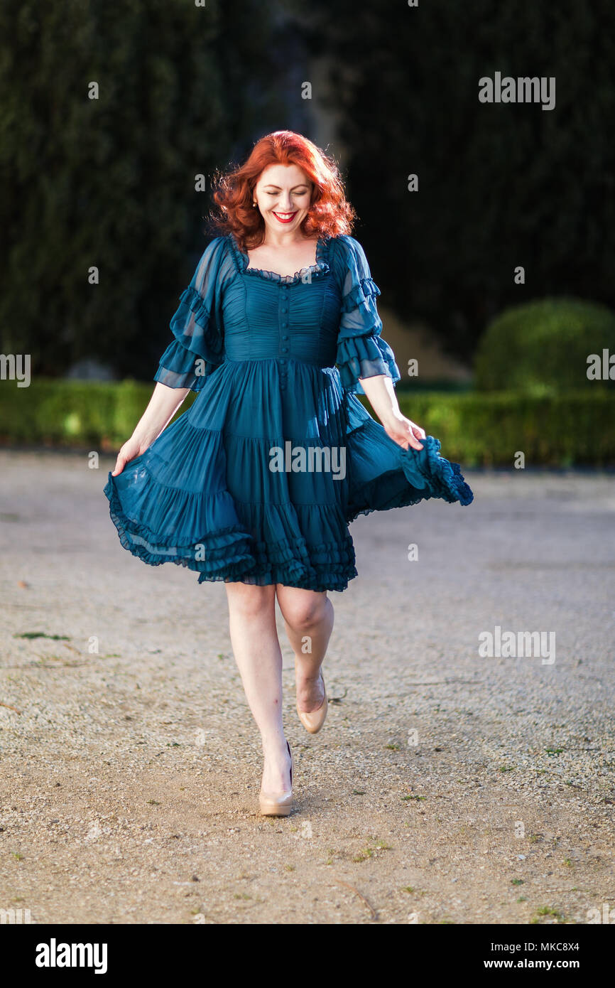 Felice redheaded donna cammina in un parco con abito fluente Foto Stock