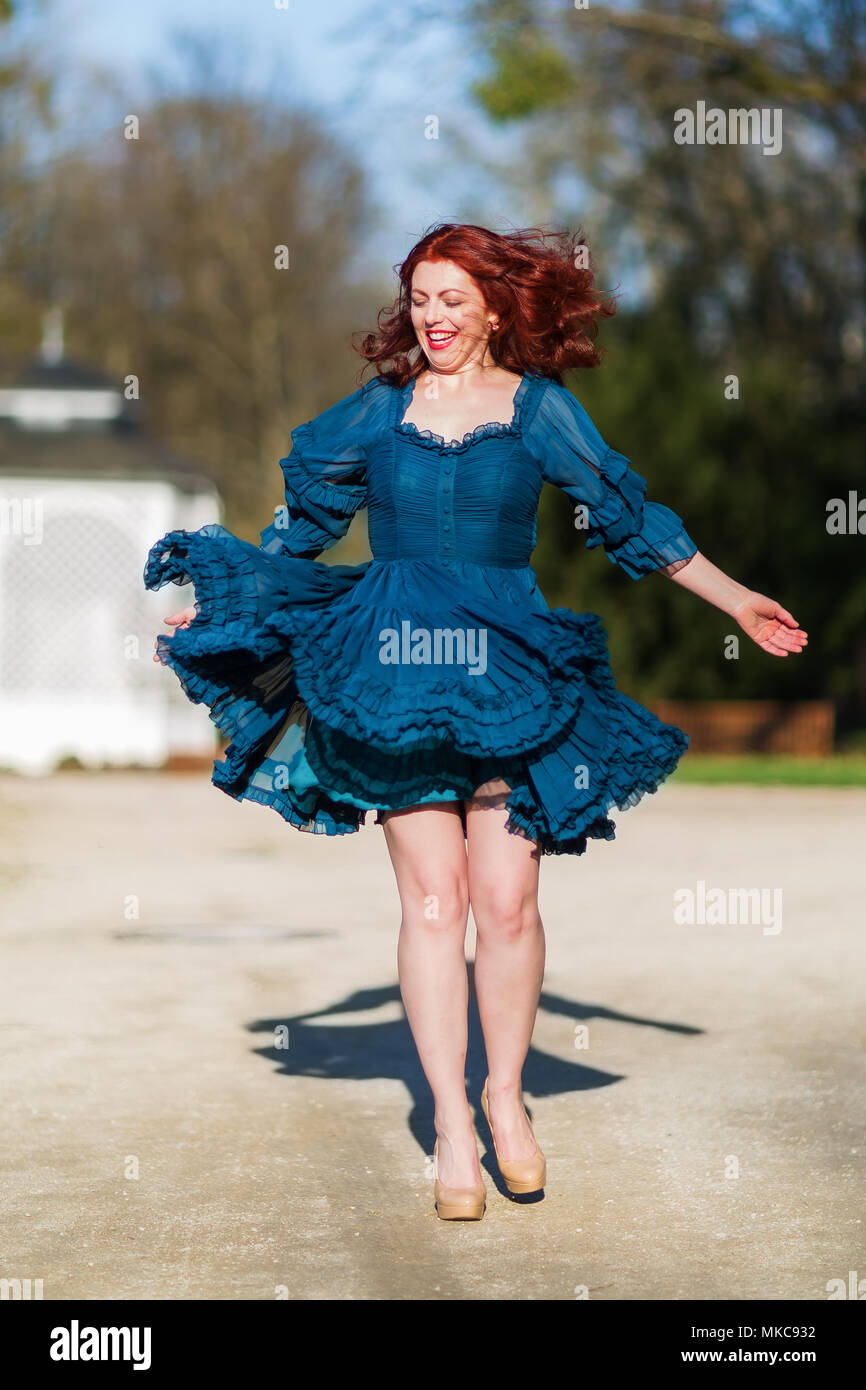 Felice redheaded donna salta in un parco con abito fluente Foto Stock