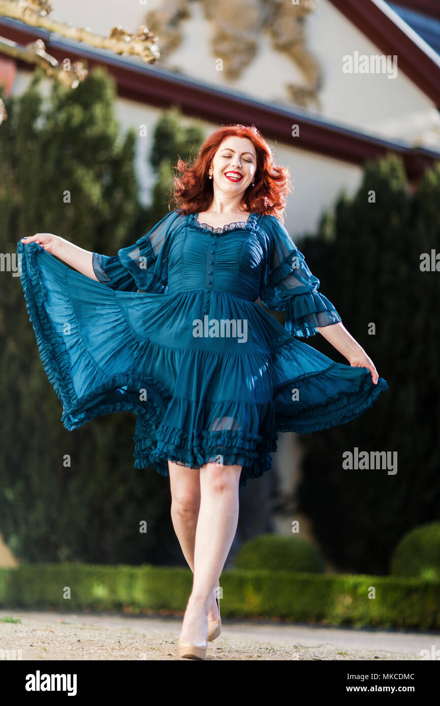 Felice redheaded donna cammina in un parco con abito fluente Foto Stock