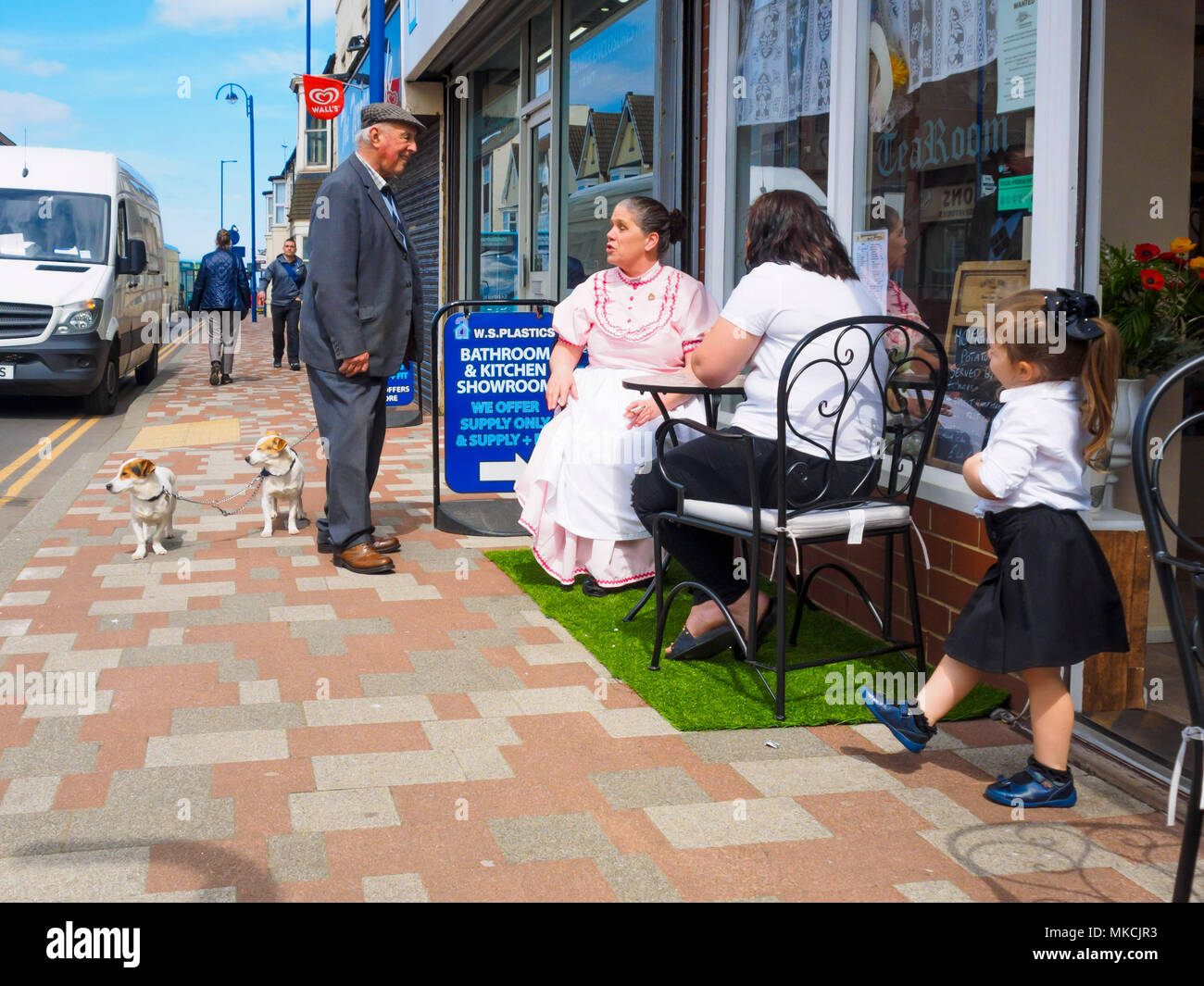 Un senior Yorkshire uomo con due cani di piccola taglia si ferma a chiacchierare con due signore e una ragazza a un tavolo esterno di un cafe in Redcar North Yorkshire Foto Stock